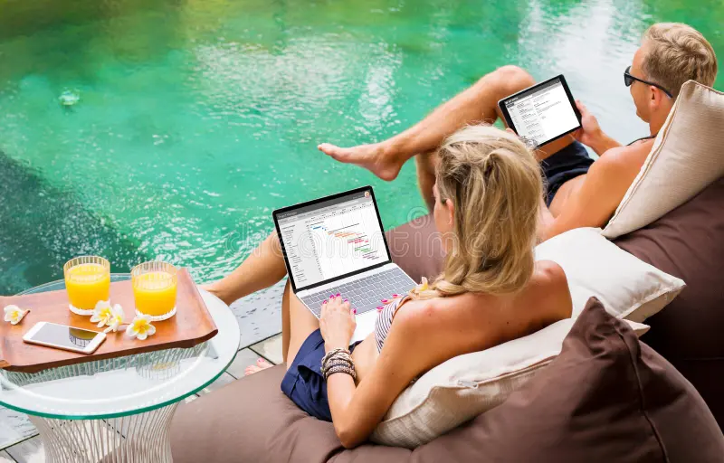 Two people working on laptops by the poolside